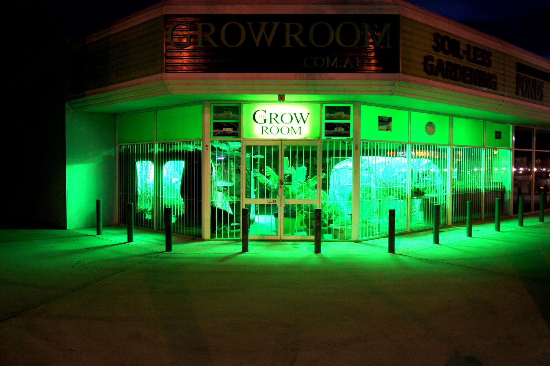 The Grow Room's corner shopfront on Albany Highway at night, glowing green with grow tents and plants visible through the windows